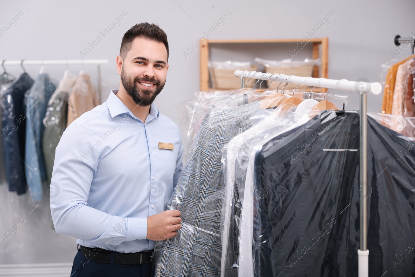 Photo of Dry-cleaning service. Happy worker taking jacket from rack indoors