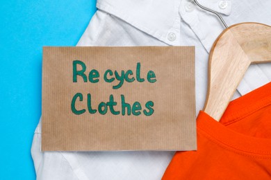 Photo of Different clothes with recycling label on light blue background, flat lay