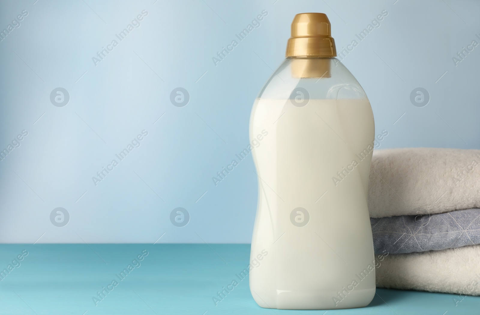 Photo of Bottle of fabric softener and towels on light blue table, space for text