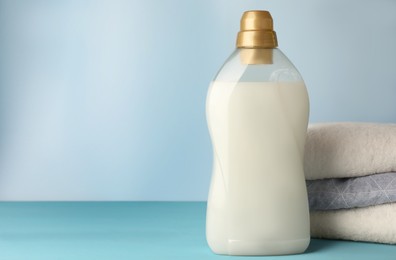 Photo of Bottle of fabric softener and towels on light blue table, space for text