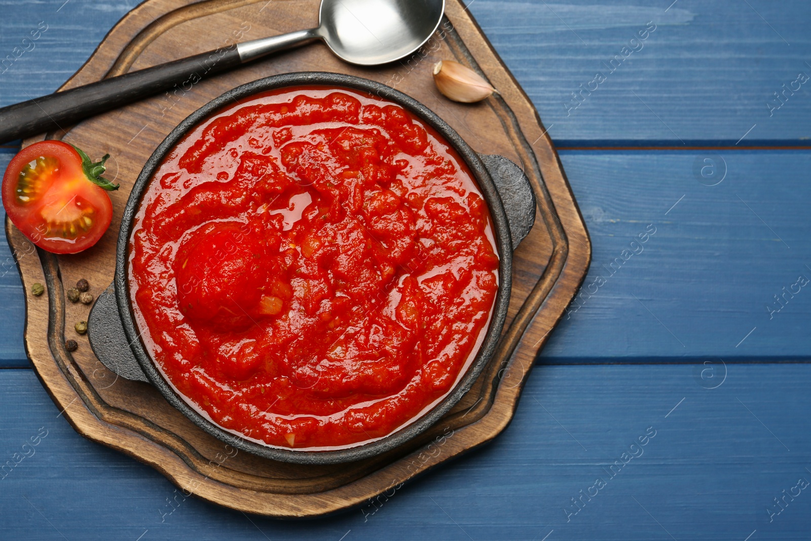 Photo of Homemade tomato sauce in bowl, spoon and ingredients on blue wooden table, top view