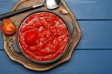 Photo of Homemade tomato sauce in bowl, spoon and ingredients on blue wooden table, top view