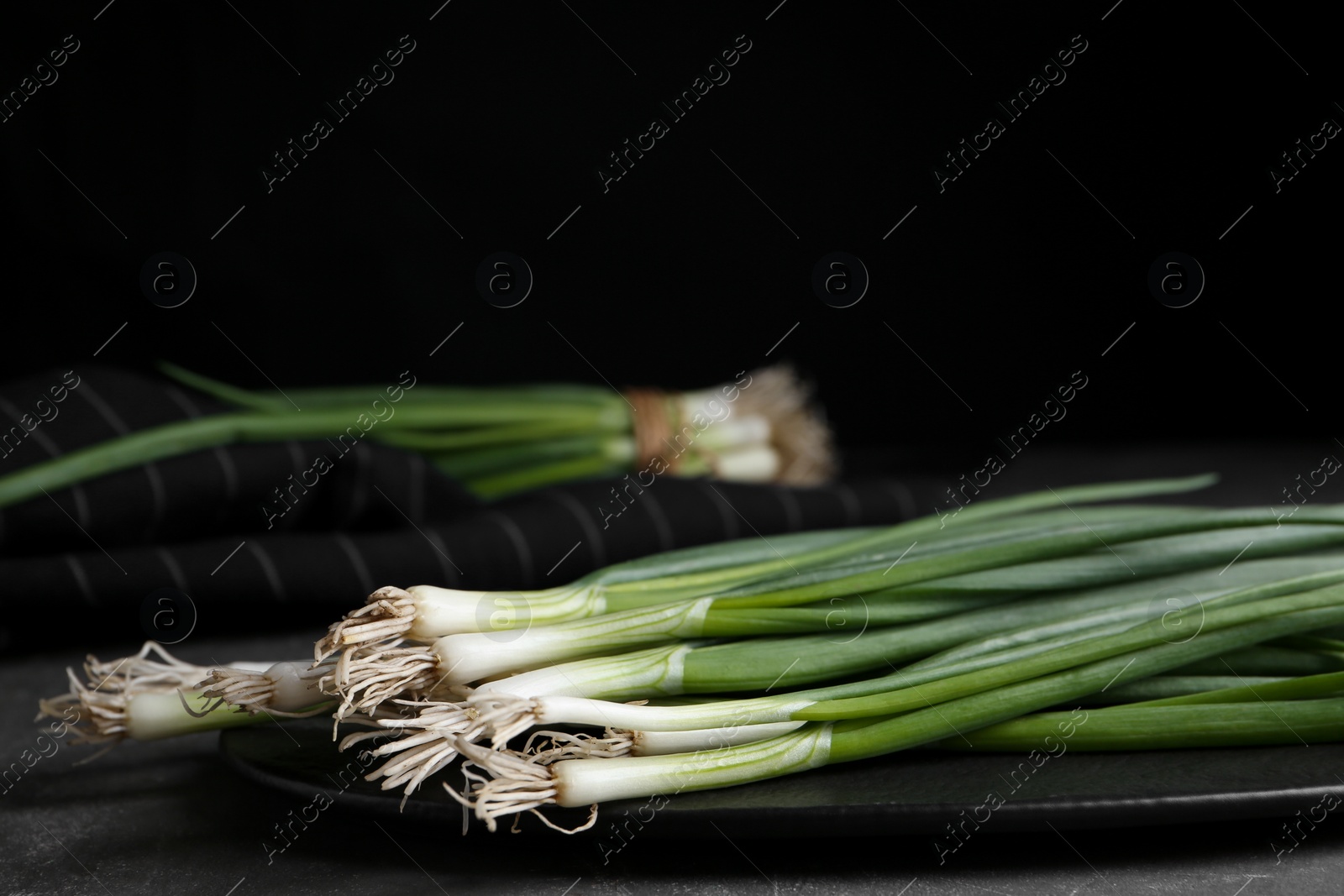 Photo of Fresh green spring onions on slate board, closeup