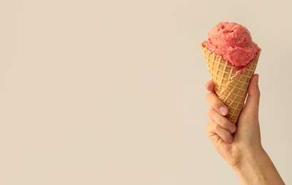 Woman holding waffle cone with delicious pink ice cream on white background, closeup. Space for text