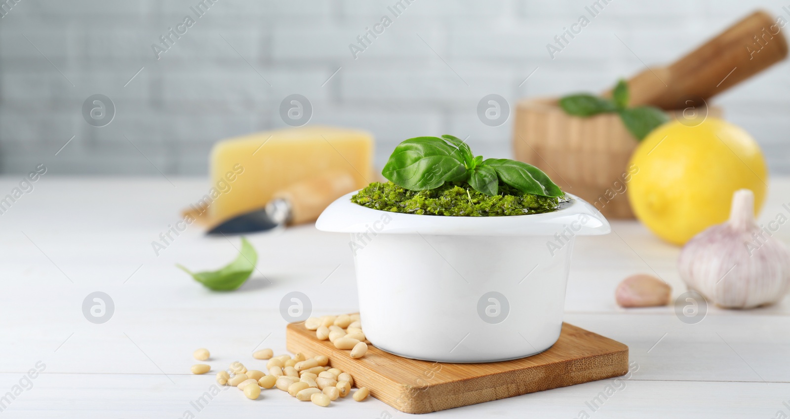 Photo of Delicious pesto sauce in bowl and ingredients on white wooden table. Space for text