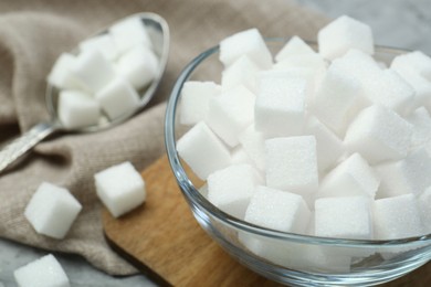 White sugar cubes in glass bowl on grey table, closeup