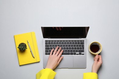 Woman with cup of coffee using laptop at light table, top view
