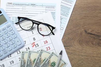 Photo of Calendar with date reminder about tax day, documents, money, calculator and glasses on wooden table, top view. Space for text