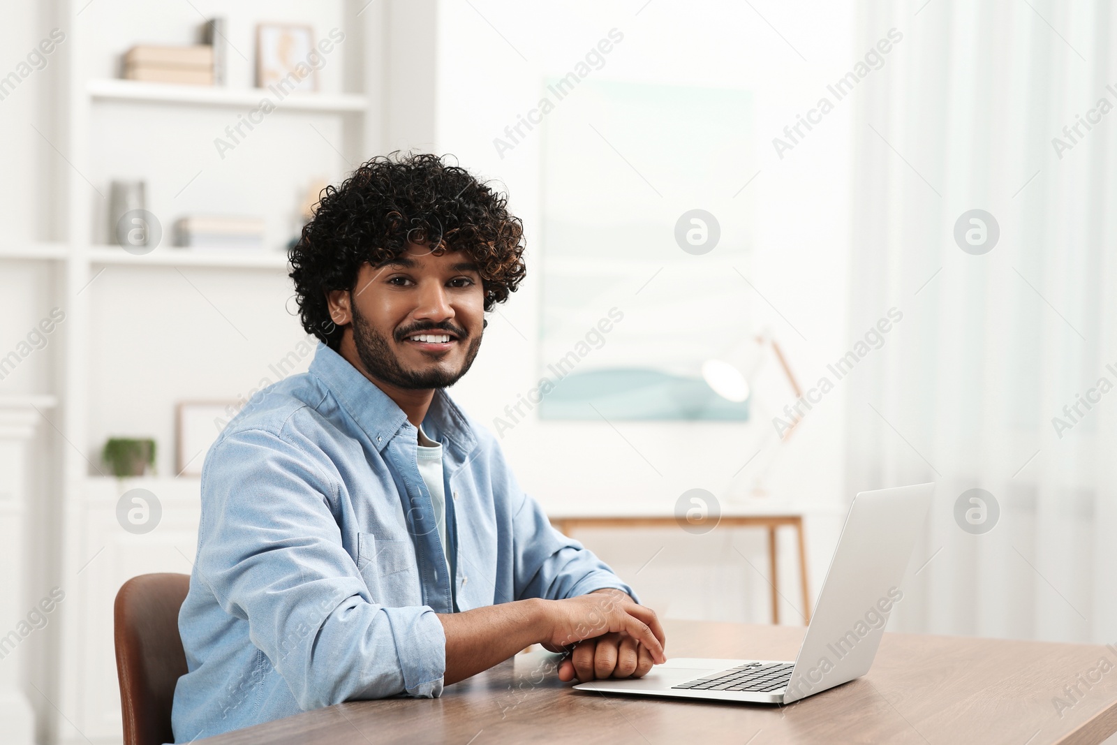 Photo of Handsome smiling man using laptop in room, space for text