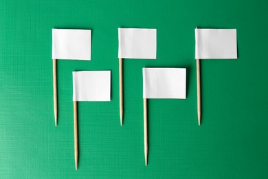 Photo of Many white paper flags on green background, flat lay