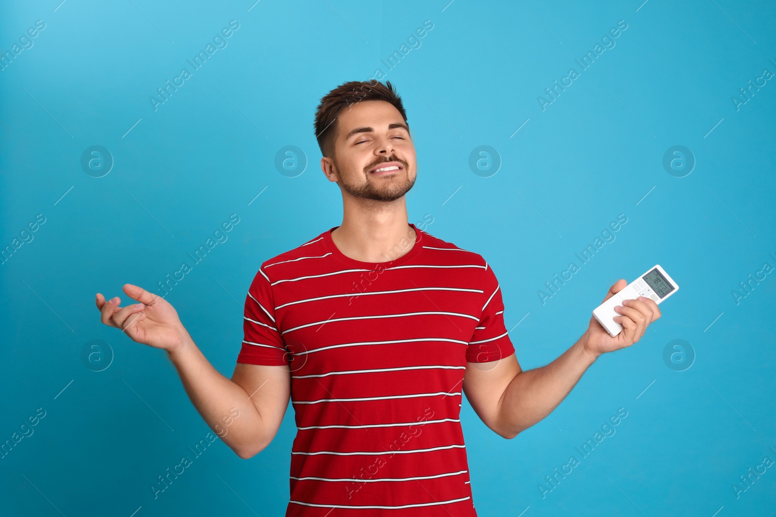 Photo of Happy young man with air conditioner remote control on light blue background