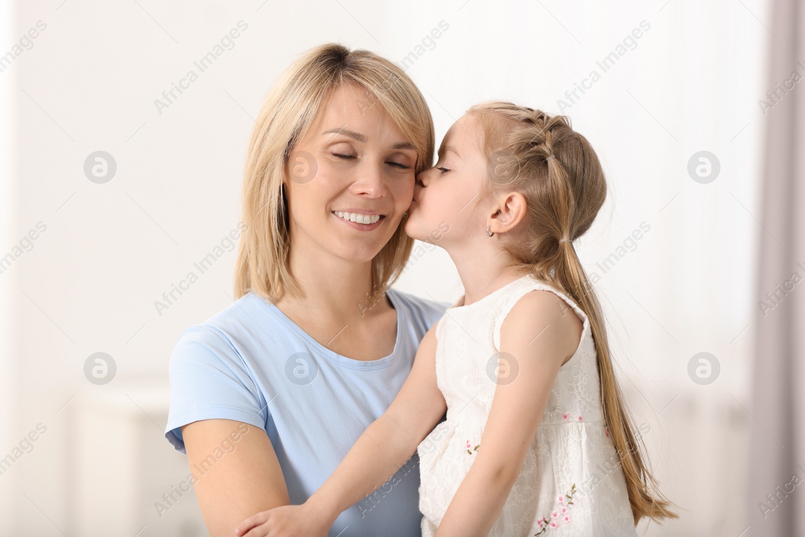 Photo of Daughter kissing her happy mother at home