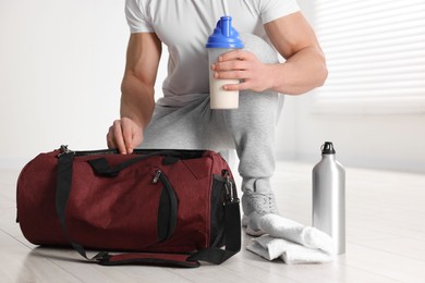 Young man putting shaker with protein into bag indoors, closeup