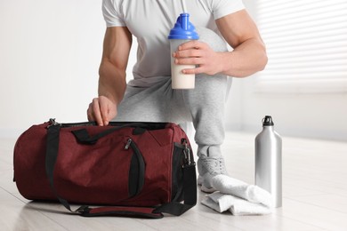 Photo of Young man putting shaker with protein into bag indoors, closeup