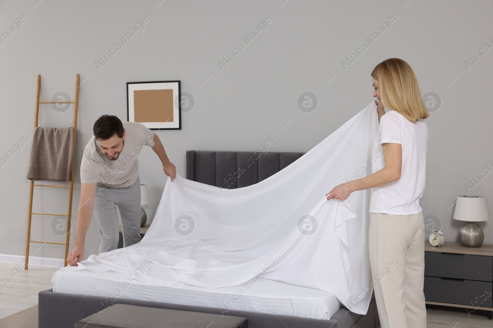 Photo of Couple changing bed linens in room. Domestic chores