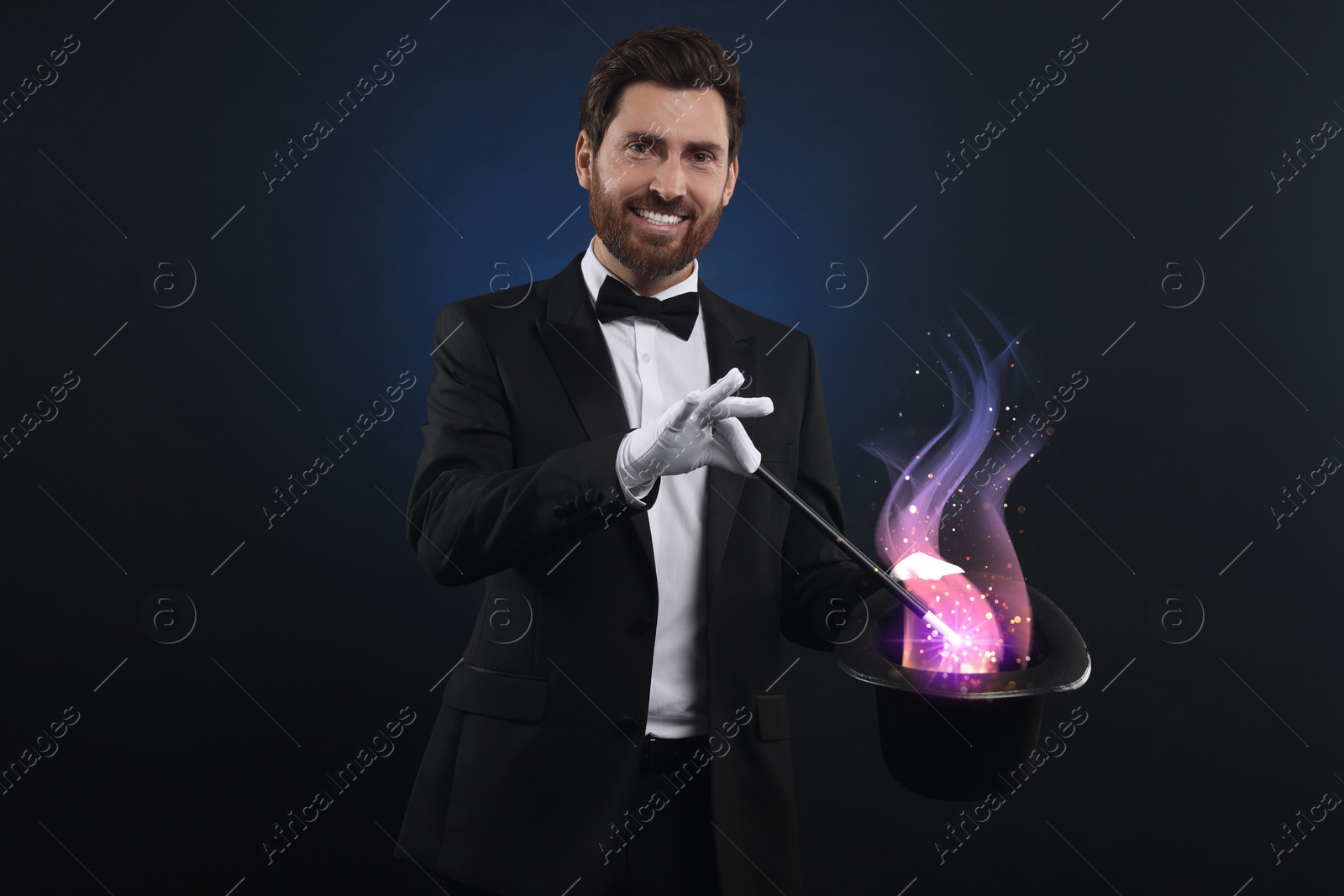 Image of Magician showing trick with wand and top hat on dark background. Fantastic light coming out of hat