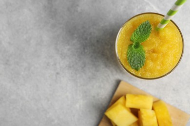 Photo of Glass of tasty pineapple smoothie with mint and cut fruit on light gray table, flat lay. Space for text