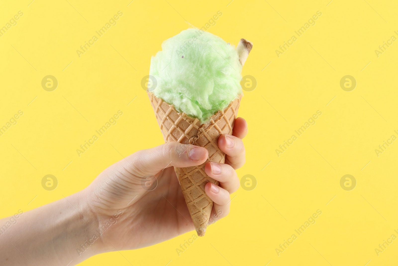 Photo of Woman holding waffle cone with cotton candy on yellow background, closeup