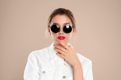 Young woman wearing stylish sunglasses on beige background