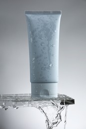 Photo of Moisturizing cream in tube on glass with water drops against grey background