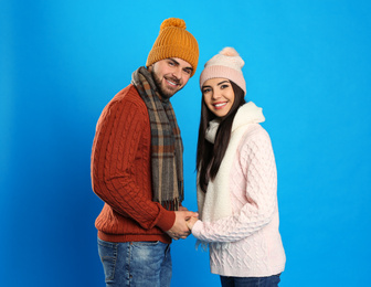 Photo of Happy young couple in warm clothes on blue background. Winter vacation