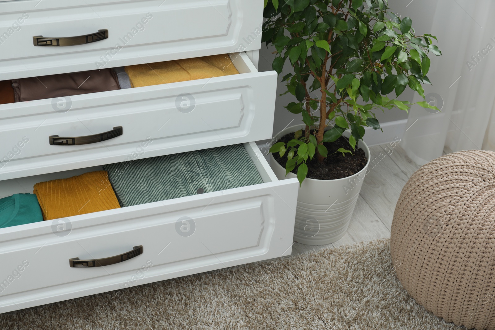 Photo of Sorting and organizing. Chest of drawers with different folded clothes indoors