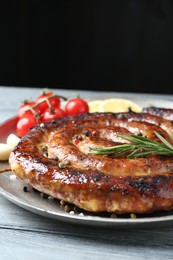 Delicious homemade sausage with spices, tomatoes and lemon on light grey wooden table against black background, closeup