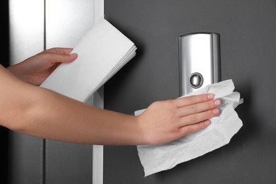 Photo of Woman cleaning elevator button with paper towel indoors, closeup