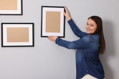 Woman hanging picture frame on gray wall