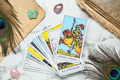 Tarot cards, old book, crystals and peacock feathers on white marble table, flat lay