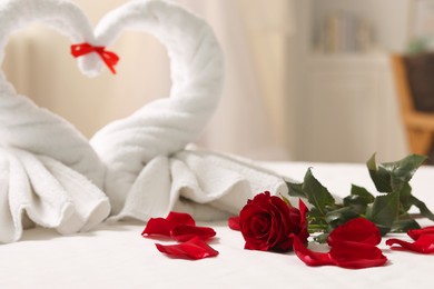 Photo of Honeymoon. Swans made of towels, rose flower and petals on bed in room, selective focus