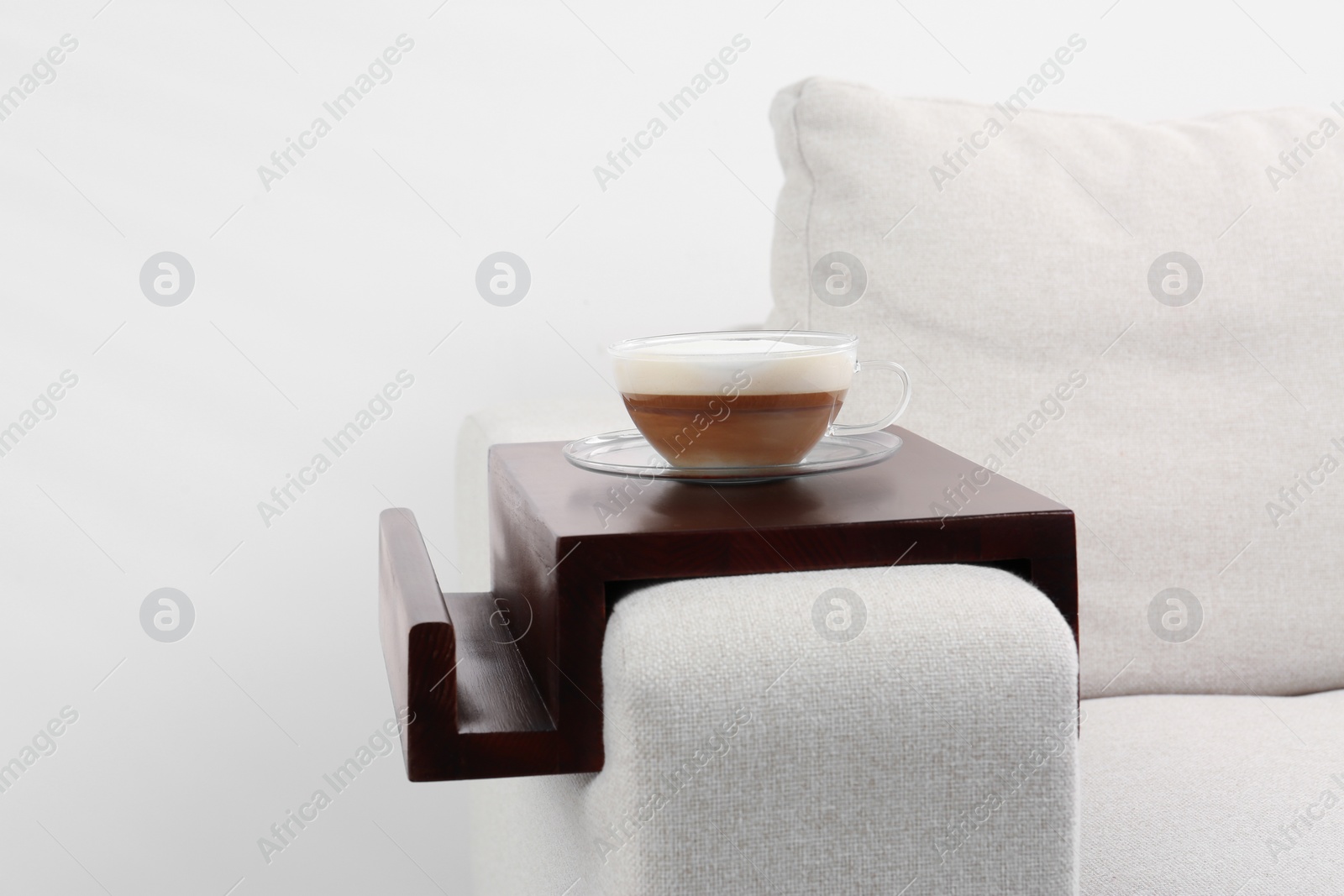 Photo of Cup of coffee on sofa with wooden armrest table indoors. Interior element