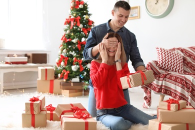 Young man surprising his girlfriend with Christmas gift at home