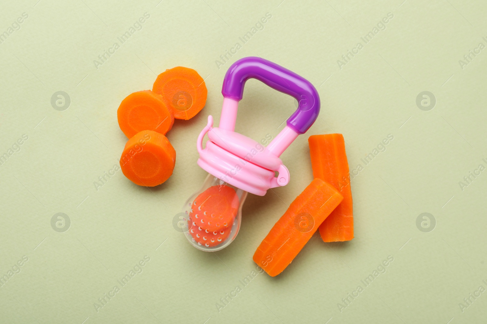 Photo of Nibbler with boiled carrot on pale green background, flat lay. Baby feeder