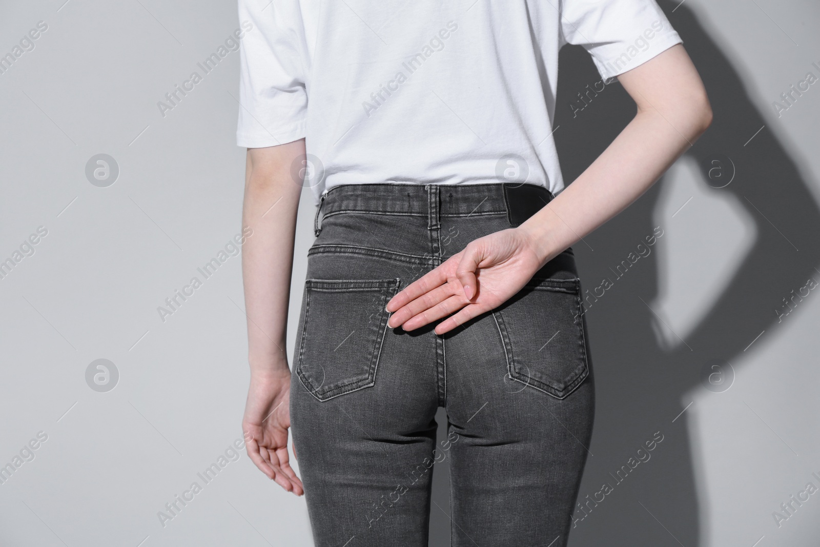 Photo of Woman showing open palm behind her back on light background, back view