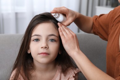 Photo of Mother using lice treatment spray on her daughter's hair indoors