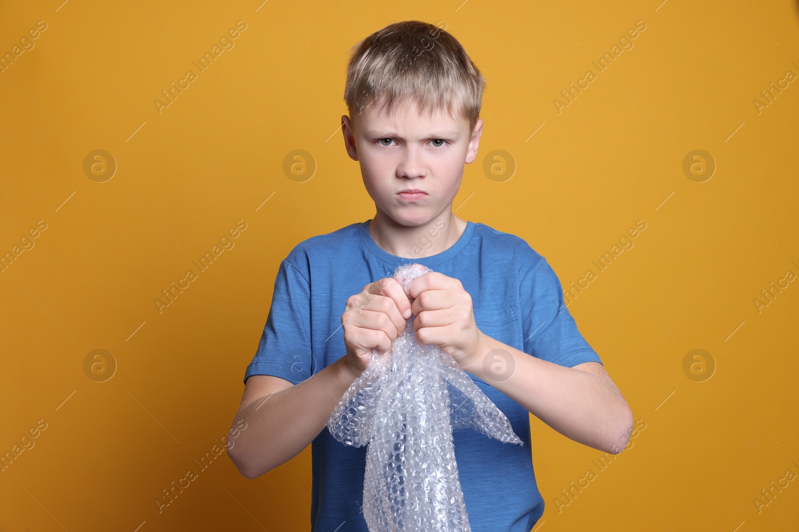 Photo of Angry boy popping bubble wrap on yellow background. Stress relief