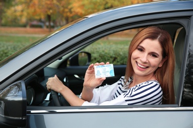 Happy woman holding driving license in car