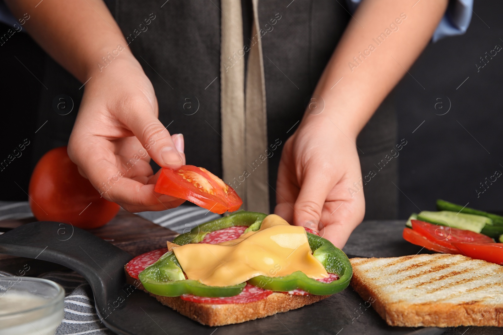 Photo of Woman adding tomato to sandwich at grey table, closeup