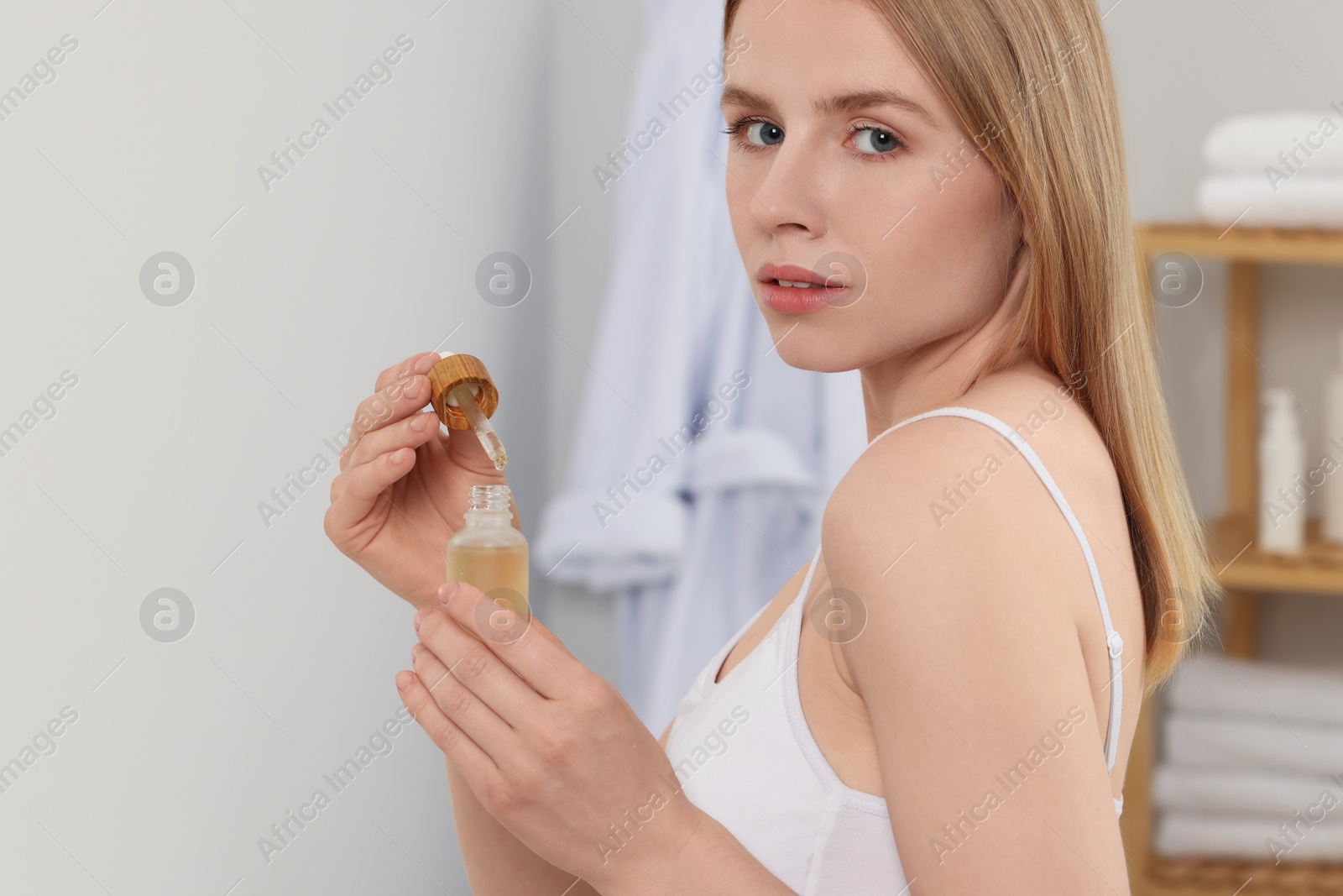 Photo of Woman with bottle of essential oil in bathroom