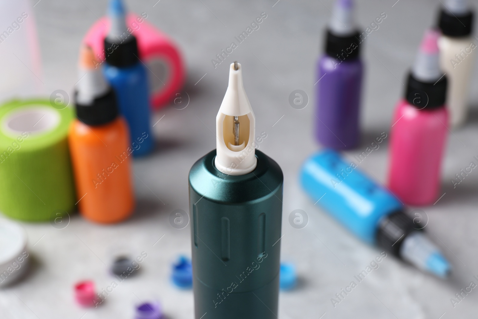 Photo of Professional tattoo machine and inks on light grey table, closeup