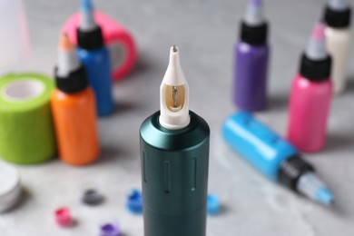 Photo of Professional tattoo machine and inks on light grey table, closeup