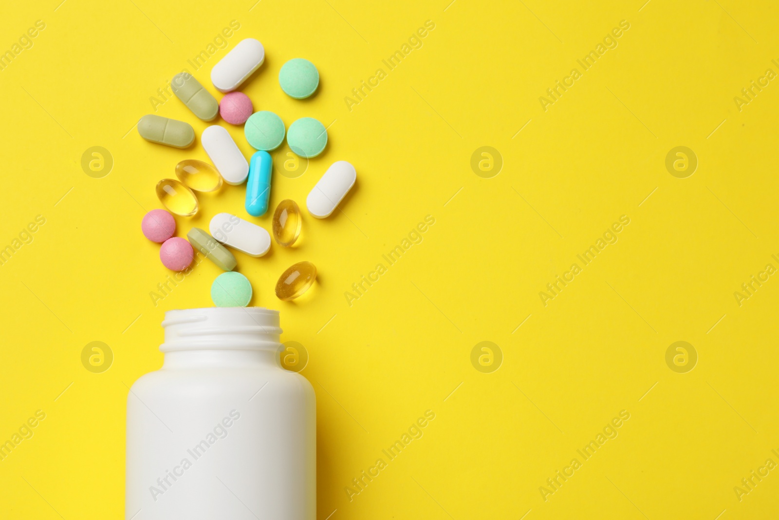 Photo of Different vitamin pills and bottle on yellow background, top view. Space for text