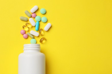 Photo of Different vitamin pills and bottle on yellow background, top view. Space for text