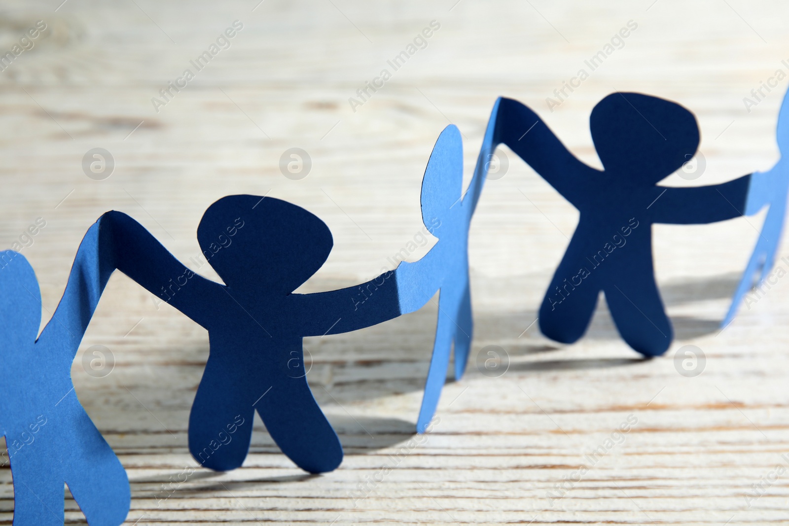 Photo of Paper people holding hands on wooden table, closeup. Unity and help concept