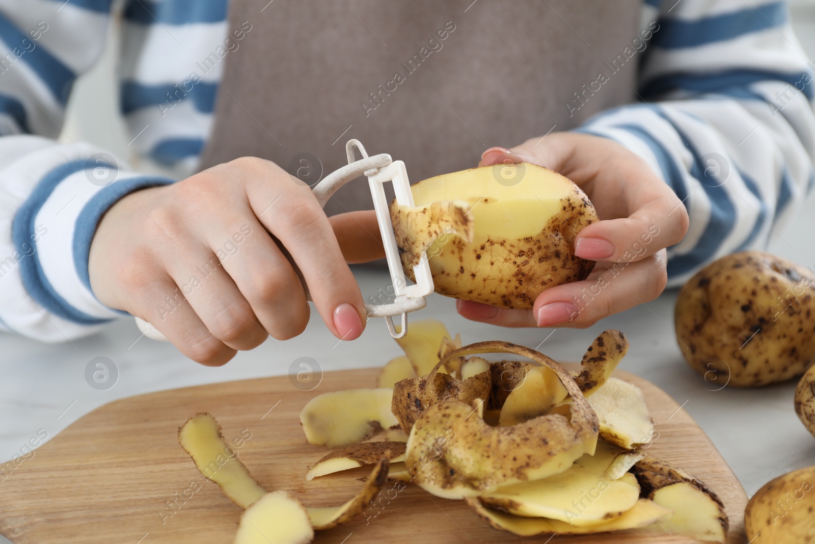 Photo of Woman peeling fresh potato at white table, closeup