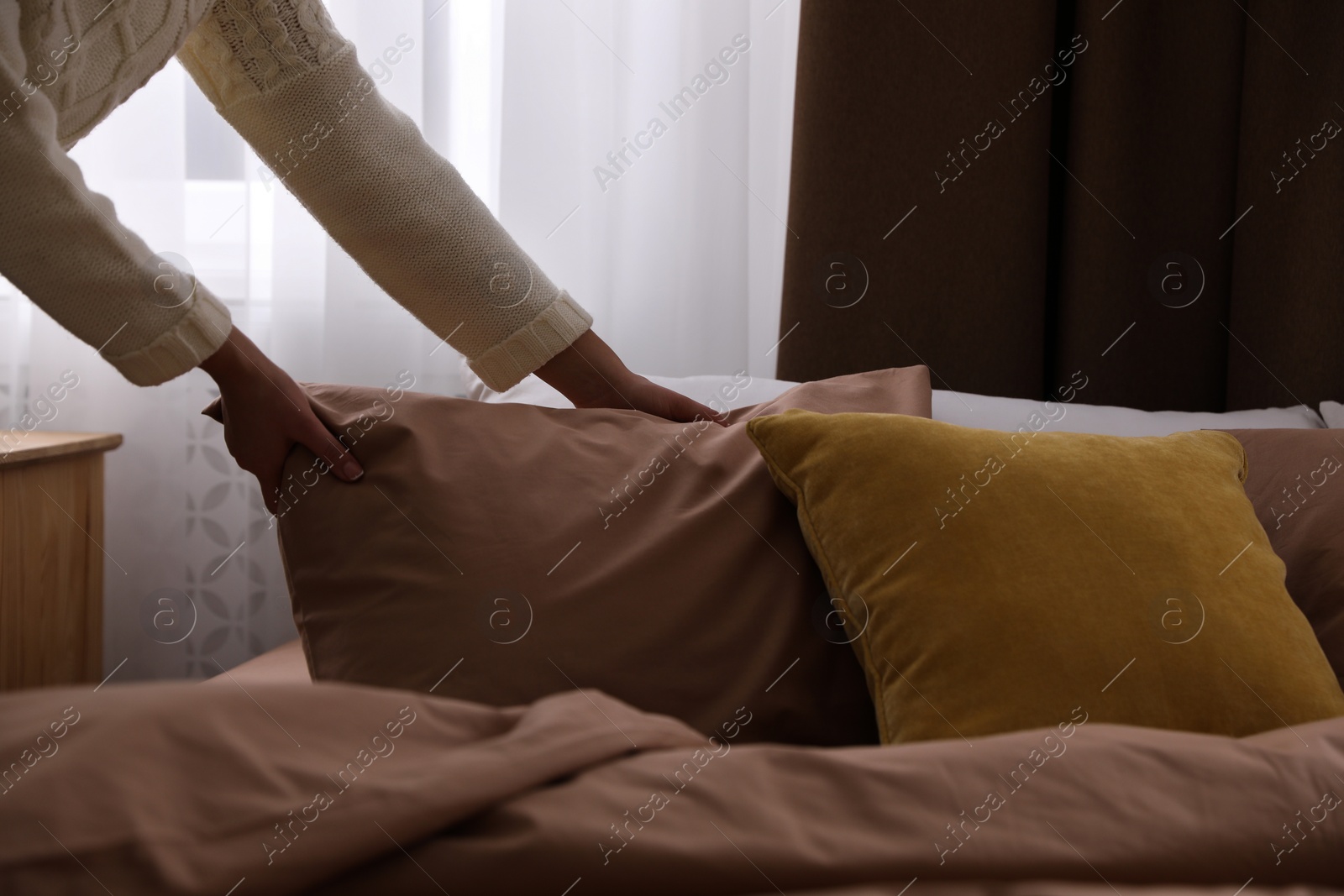 Photo of Woman making bed with brown linens, closeup