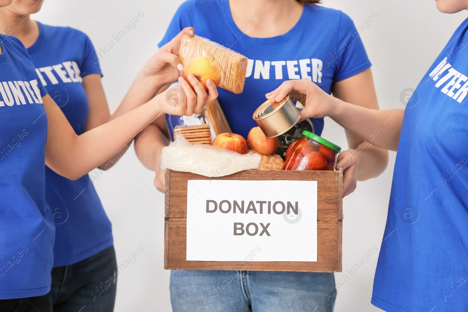 Photo of Volunteers putting food products in donation box on light background