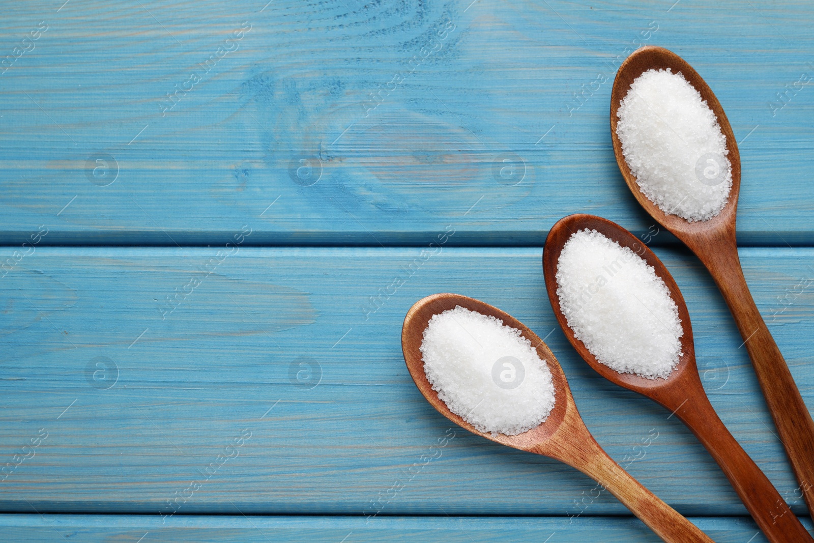 Photo of Granulated sugar in spoons on turquoise wooden table, flat lay. Space for text