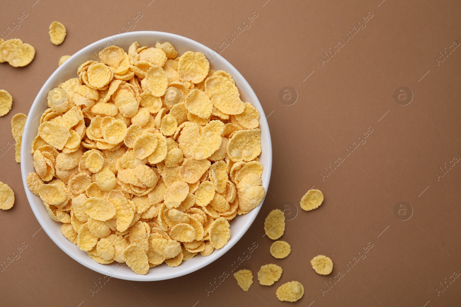 Photo of Breakfast cereal. Tasty corn flakes in bowl on brown table, top view. Space for text